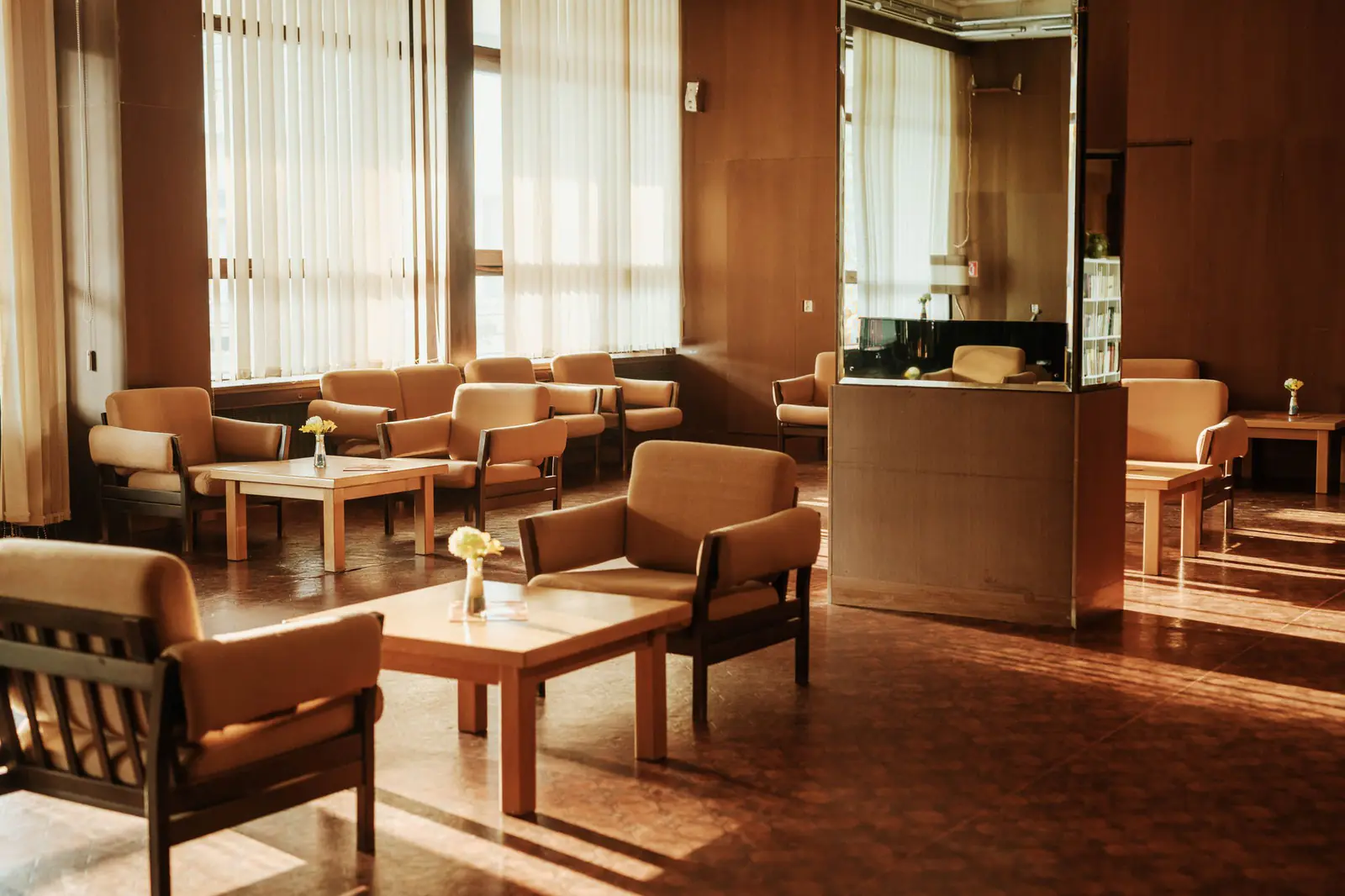 Sala de espera com poltronas de tecido claro e luz quente de fim de tarde entrando pelas persianas
